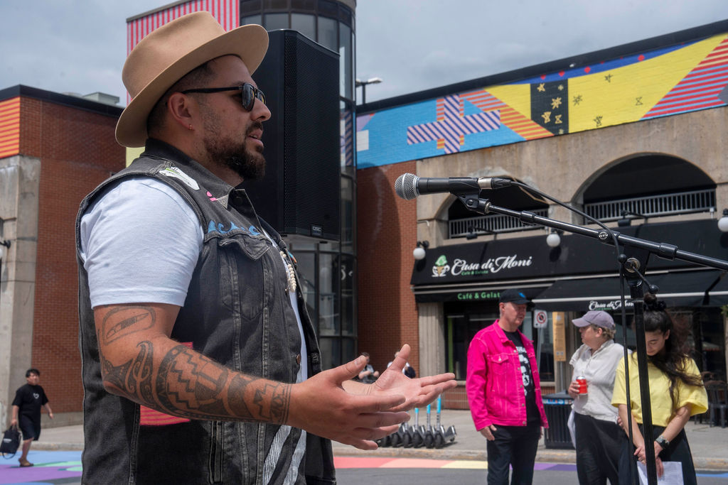 Jordan Bennett speaking in front of his colourful mural on the Clarence Street parking garage in downtown Ottawa.